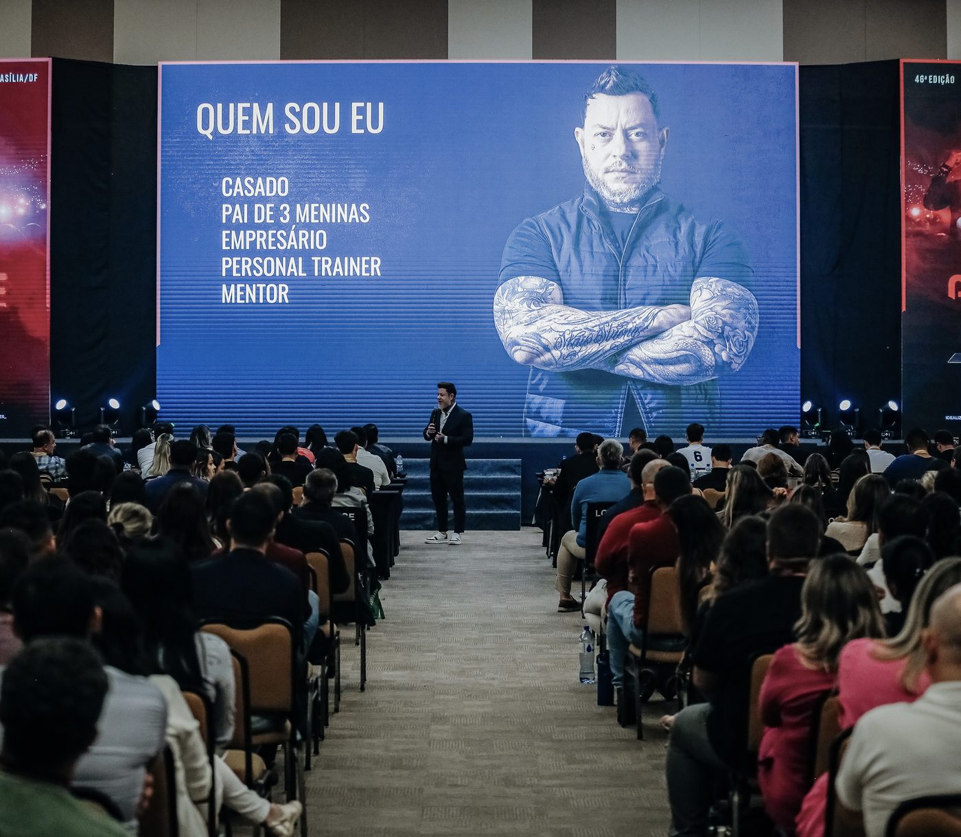 Greg Pàz palestrando em auditório lotado.